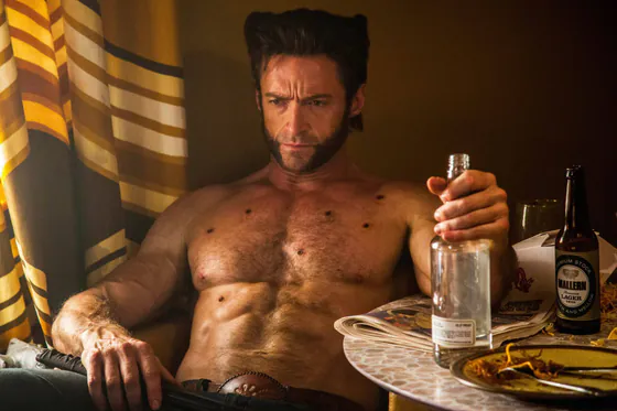 Shirtless man sitting at a table holding an empty bottle